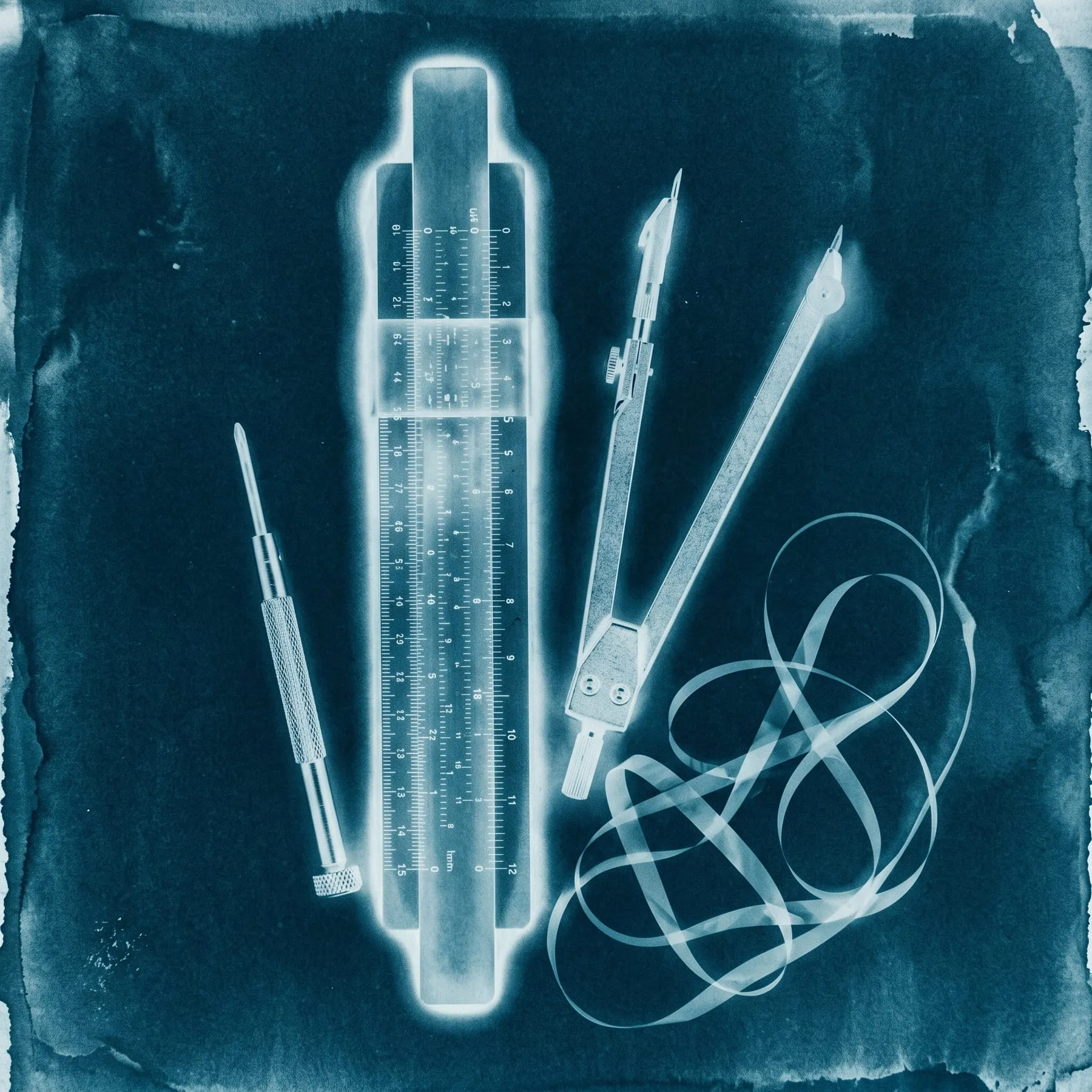 A photogram of a slide rule, a compass, a screwdriver and a loop of tape laid out like tools on a bench, toned cyan.