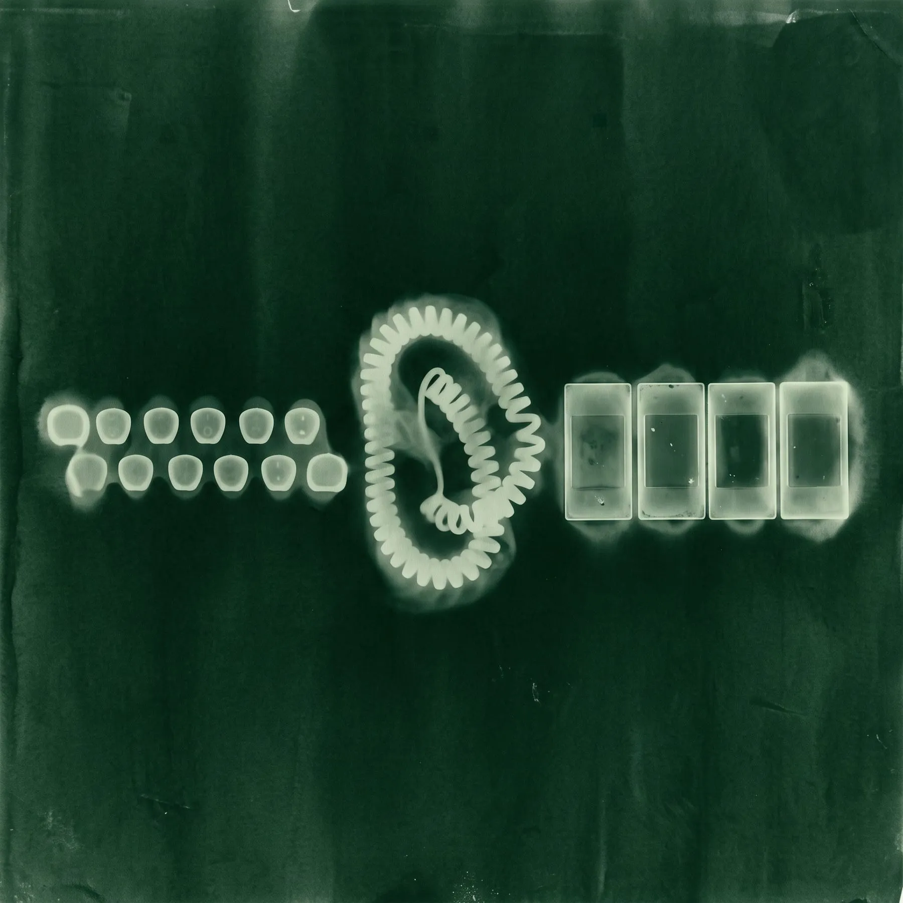 A photogram of typewriter keycaps, a coiled cord and four glass slides side by side, toned bottle green.